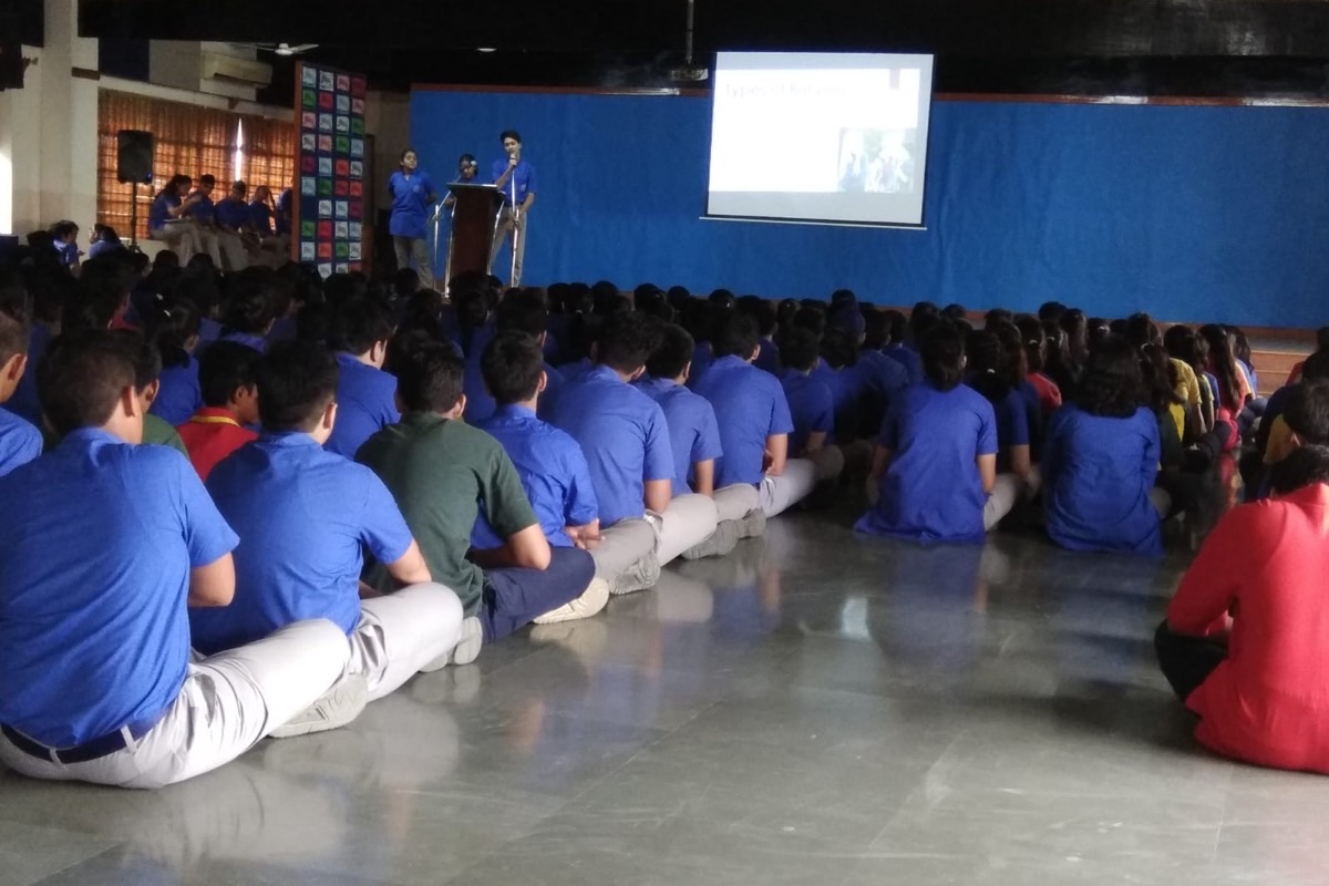Students seated across the floor of a school assembly hall during a workshop on bullying, with the presentation on screen behind the stage